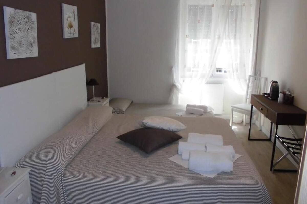 Une chambre d’hôtel bien rangée, avec un lit, des oreillers, une table de chevet et un bureau avec une chaise.