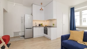 A modern kitchen with white cabinets, a built-in oven, and a coffee maker. There is a blue sofa with a yellow pillow in the living area. - ShortStayPoland Rakowiecka B179 (Warsaw)
