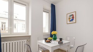 A room with a white table, clear chairs, a radiator, a window with a view of buildings, and a framed picture on the wall. - ShortStayPoland Rakowiecka B179 (Warsaw)