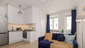 A modern kitchen with white cabinets, a stove, and a sink. There is a blue sofa with cushions and a lamp to the right. - ShortStayPoland Rakowiecka B179 (Warsaw)