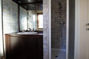 A bathroom with a wooden vanity, a white sink, and a shower with a tiled wall. - Ungheria 25 (Udine)