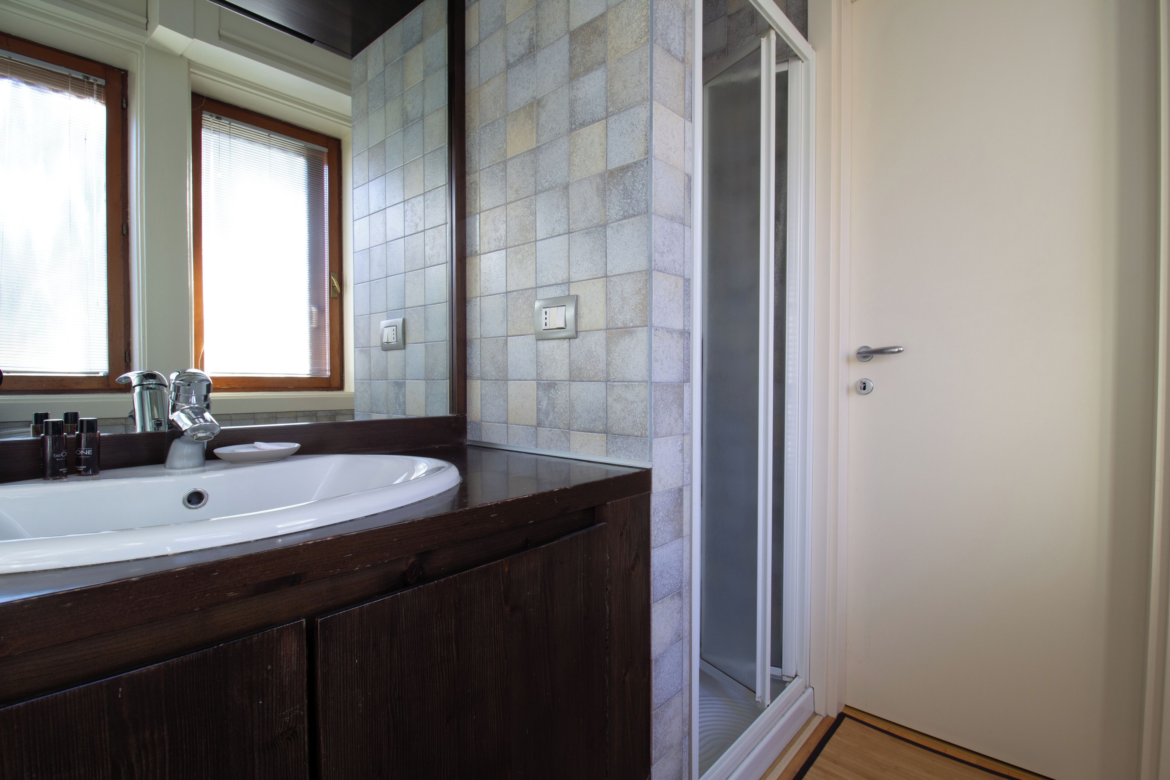 Un baño con un lavamanos grande de color blanco, tocador de madera oscura, paredes con azulejos y una puerta de ducha de vidrio.