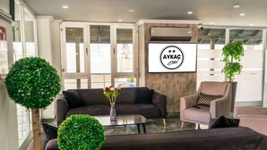 A modern hotel lobby with a dark-colored sofa, a glass coffee table, and a potted plant. - Aykaç Otel Susanoğlu (Silifke)