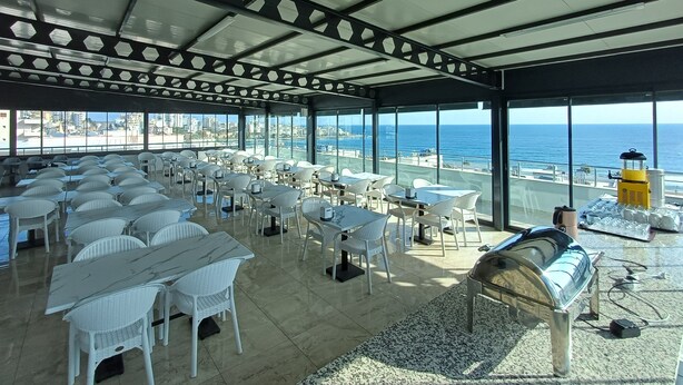 A rooftop restaurant with white tables and chairs, a buffet area, and a view of the ocean. - Aykaç Otel Susanoğlu (Silifke)