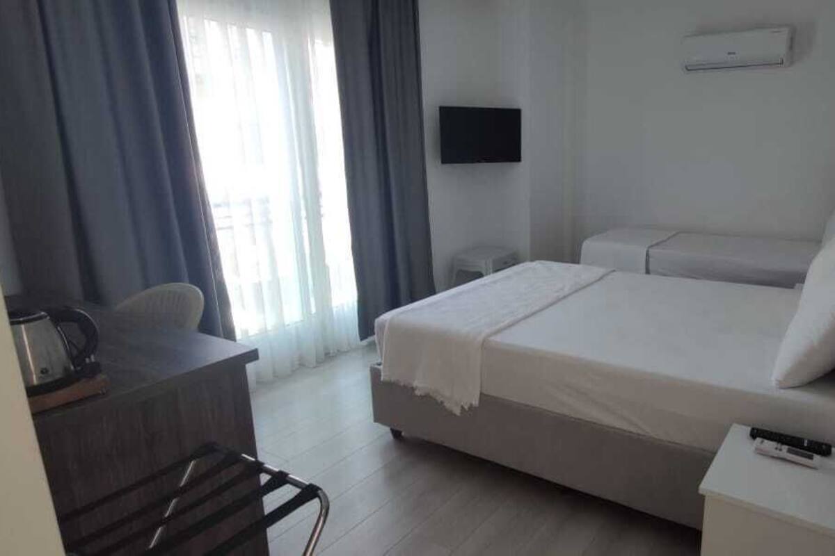 A hotel room with a bed, a desk with a chair, a TV, and a window with curtains.
