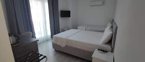 Habitación de hotel con cama, escritorio con silla, televisión y ventana con cortinas.