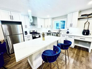 A modern kitchen with white cabinetry, stainless steel appliances, a central island with bar stools, and a large window providing natural light. - Spring Valley 2BR | Sleeps 6, Pets OK, AC and WiFi (Spring Valley)