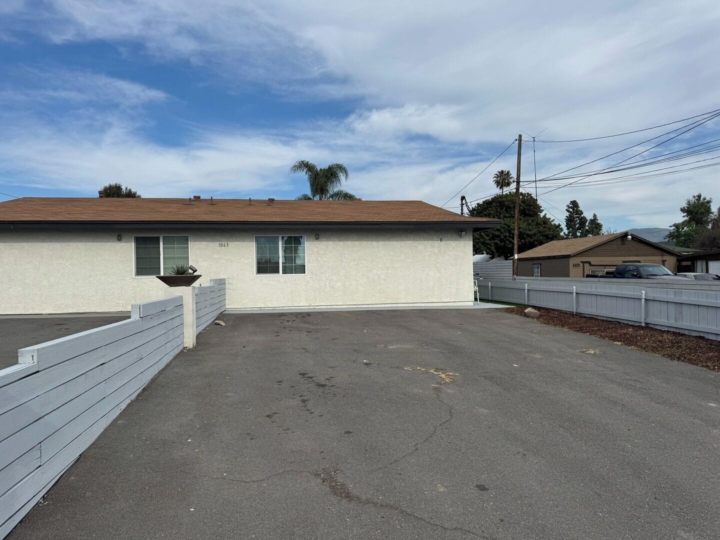 A single-story building with a flat roof, a small parking area, and a white fence.