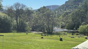Een begroeid veld met verspreide objecten en bomen, een heuvel met weelderige vegetatie, en een heldere lucht.