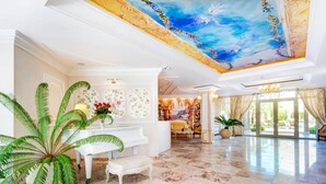 A grand lobby with a piano, a large fern plant, and a mural on the ceiling. - Marino Mar | Boutique Apartment | Spa & Wellness, pools, sun loungers included (Sunny Beach)