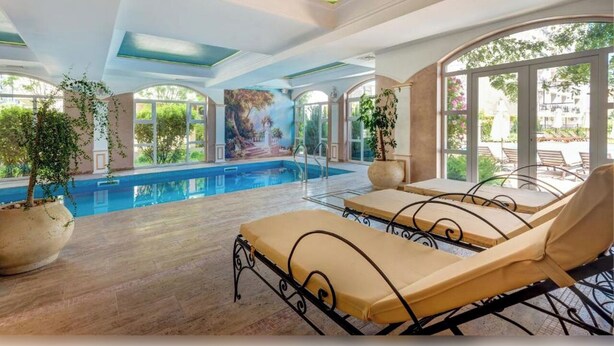 An indoor swimming pool with lounge chairs, large windows, and a mural on the ceiling. - Marino Mar | Boutique Apartment | Spa & Wellness, pools, sun loungers included (Sunny Beach)