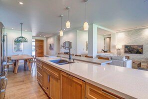 A modern kitchen with a large island, wooden cabinetry, pendant lighting, and a stone accent wall.