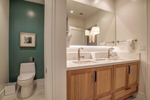 Un baño moderno con inodoro blanco, un espejo grande y un tocador de madera con dos lavamanos.