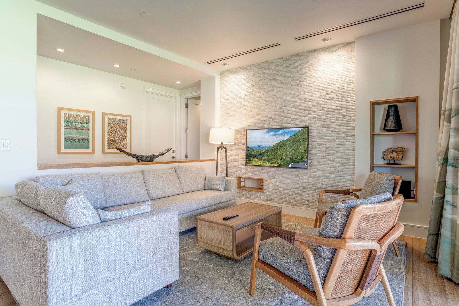 A living room with a sofa, armchair, coffee table, and a TV mounted on a textured wall.