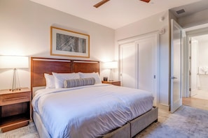 Un dormitorio ordenado con cama, mesitas de noche, una obra de arte enmarco y un armario.