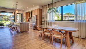 A modern kitchen with wooden cabinets, a stainless steel refrigerator, and a dining area with a glass table and chairs. - Honua Kai | Ocean View 6 BR, Sleeps 16 | Car Incl. w/ 6+ Nights | HKL ML-1099 by KBM (Lahaina)