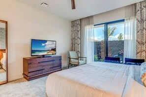 Un dormitorio con una cama grande, un televisor en una cómoda, una silla y vistas al océano a través de amplios ventanales.