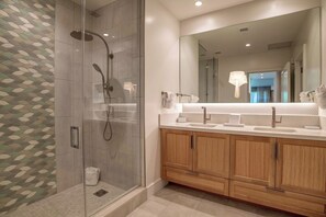 Un baño moderno con ducha de vidrio, un espejo grande y armarios de madera.