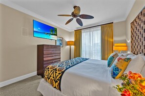 A hotel room with a bed, ceiling fan, TV, and a window with curtains.