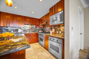 A modern kitchen with wooden cabinets, a granite countertop, stainless steel appliances, and a stone backsplash.