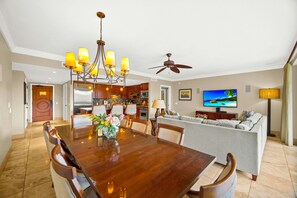 A spacious living area with a dining table, sofa, TV, and ceiling fan.