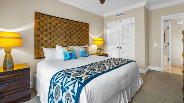 A bedroom with a large bed, a ceiling fan, a wooden headboard, two bedside lamps, and a door. - Honua Kai | Ocean View 6 BR, Sleeps 16 | Car Incl. w/ 6+ Nights | HKH ML-1097 by KBM (Lahaina)