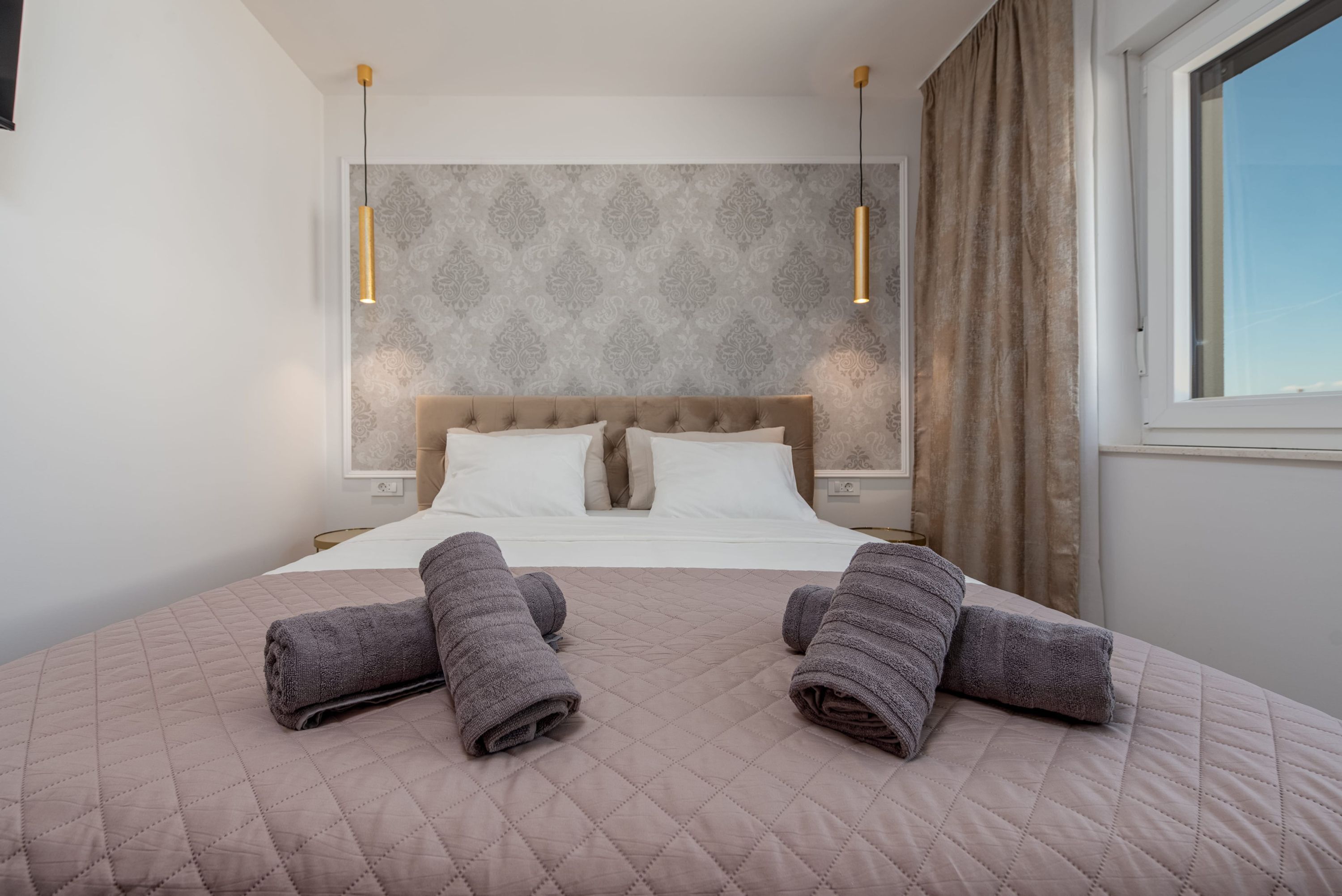 A neatly made bed with a quilted headboard, two bedside tables, and two wall-mounted lamps.