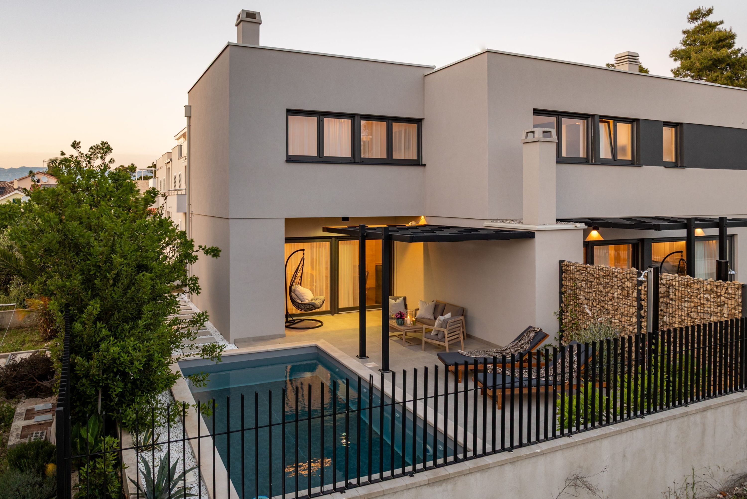 A modern two-story house with a swimming pool, outdoor seating, and a covered patio area.