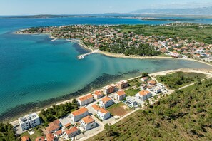 Luftaufnahme einer Küstenstadt mit Wohnhäusern, einem Strand und klarem, blauem Wasser.