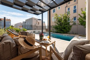 Ein überdachter Außenbereich mit Pool, Liegestühlen und einem Tisch mit Buch und Getränk.
