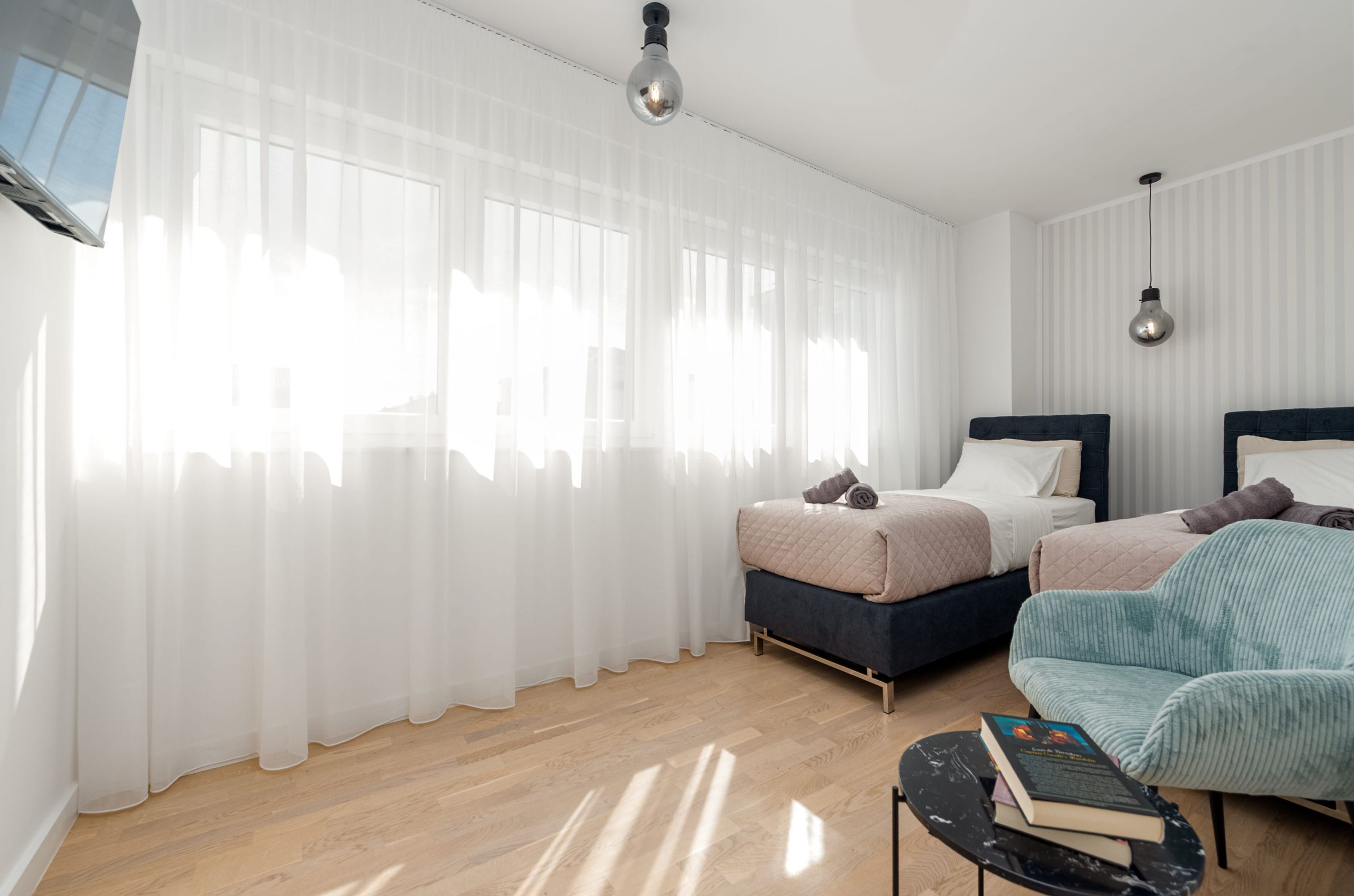 A modern bedroom with two beds, sheer curtains, and a wooden floor.