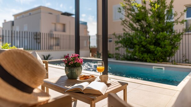 A poolside setting with a table, a book, a glass of orange juice, and a bowl of food. - Villa Mia Zadar Villas (Privlaka)