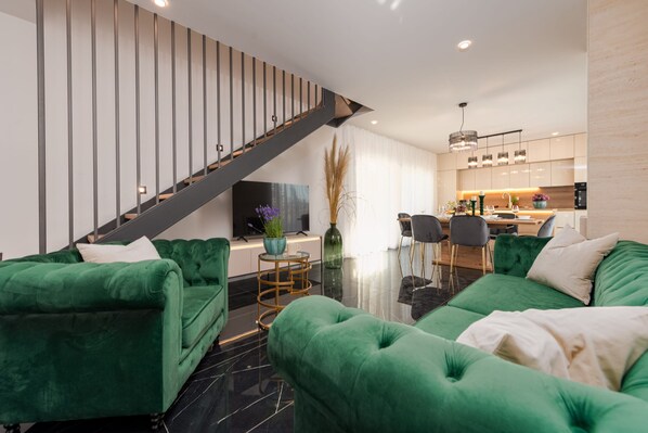 Una sala moderna con un juego de sofá verde, un comedor con una mesa y sillas de madera, y una cocina con una isla central.