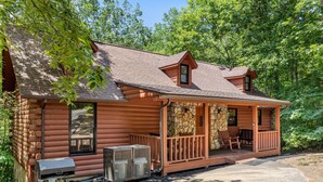 A log cabin with a stone porch, a small deck, and a covered outdoor seating area.