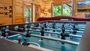 A foosball table in a room with wooden walls and a large window.