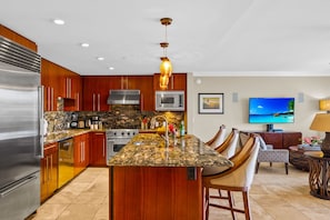 A modern kitchen with a central island, stainless steel appliances, and a flat-screen TV mounted on the wall.
