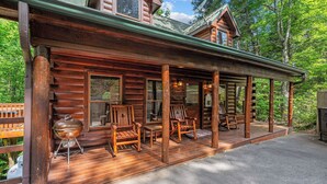 A log cabin with a porch, wooden chairs, a grill, and a wooden deck. - A Home For The Whole Family, Even The Family Dog (GATLINBURG)