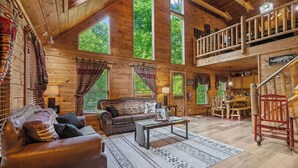 A rustic cabin interior with a wooden staircase, a sofa, a coffee table, and large windows. - A Home For The Whole Family, Even The Family Dog (GATLINBURG)