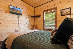 Een houten kamer met een bed, een wandgemonteerde televisie, een raam met zonwering en een ingelijste foto aan de muur.