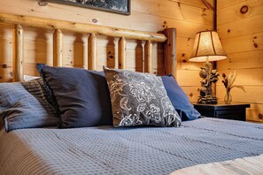 L'intérieur d'une cabane en bois, avec un lit, des oreillers, une table de chevet et une lampe.