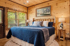Quarto de cabana de madeira com uma cama, duas luminárias de cabeceira, um quadro na parede e uma janela com persianas.