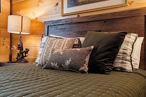 Een bed met een gewatteerde groene spreideken, een houten hoofdbord en drie kussens met verschillende patronen.