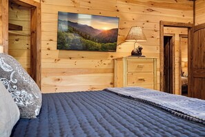 Une chambre dans un chalet en bois, avec un lit, une table de chevet, une lampe et un tableau représentant un paysage forestier.