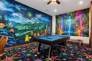 Quarto com mesa de bilhar, um mural com cena noturna e personagens, e um mural em formato de cascata.