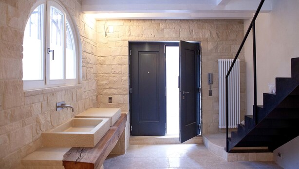 A modern bathroom with a stone wall, a large window, a sink, and a dark door. - La casa di Valbelluna (Feltre)