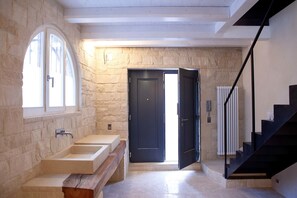 A modern bathroom with a stone wall, a large window, a sink, and a dark door. - La casa di Valbelluna (Feltre)