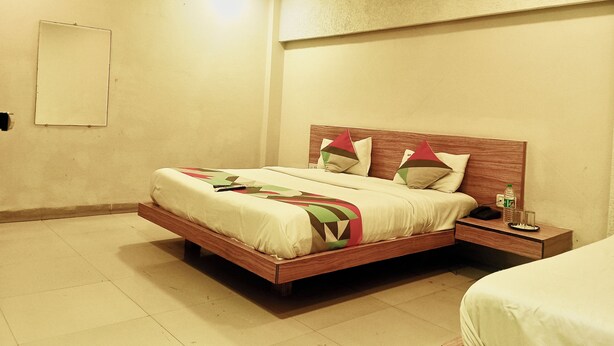 A bedroom with a wooden bed, a nightstand, a ceiling fan, and a wall-mounted light fixture. - Hote SVL (Indore)
