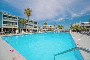 Une piscine avec des chaises longues et un immeuble à plusieurs étages doté de balcons.
