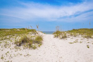 Un sentier de sable qui longe la plage et mène à la mer, avec des dunes de chaque côté.