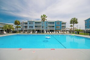 Una piscina con sillas de descanso y un edificio con balcones al fondo.